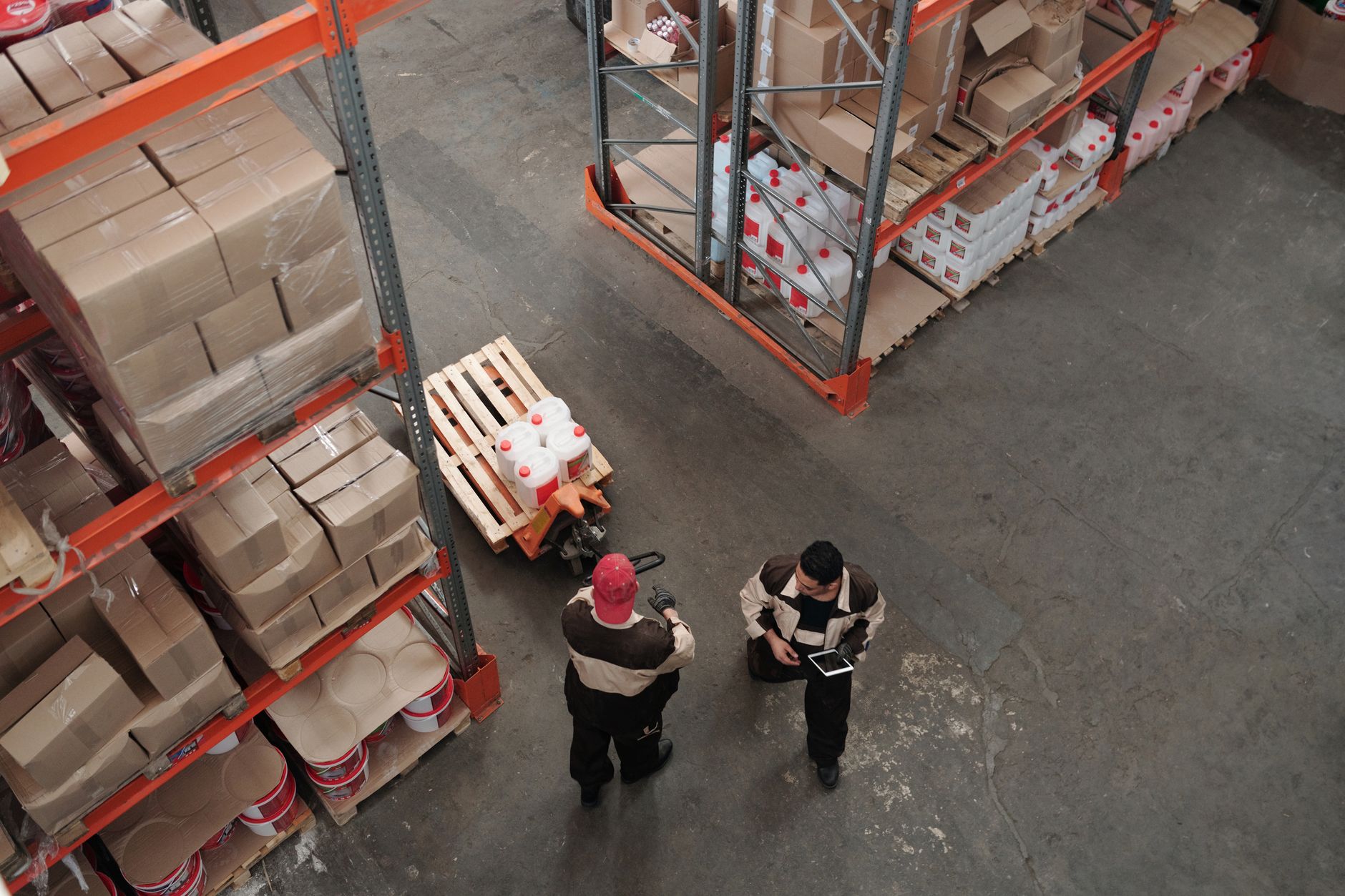 Warehouse workers organizing inventory on pallets and shelving from an overhead angle