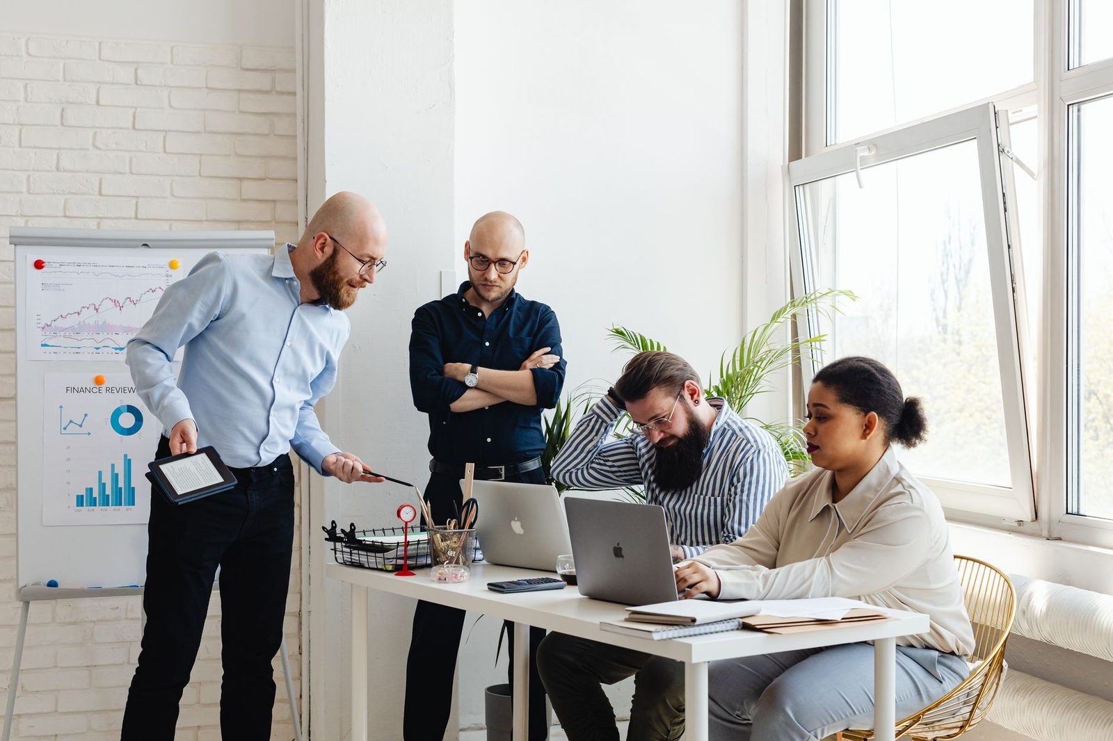 A small team gathered around a laptop and printed charts, discussing IT strategy together in a modern office