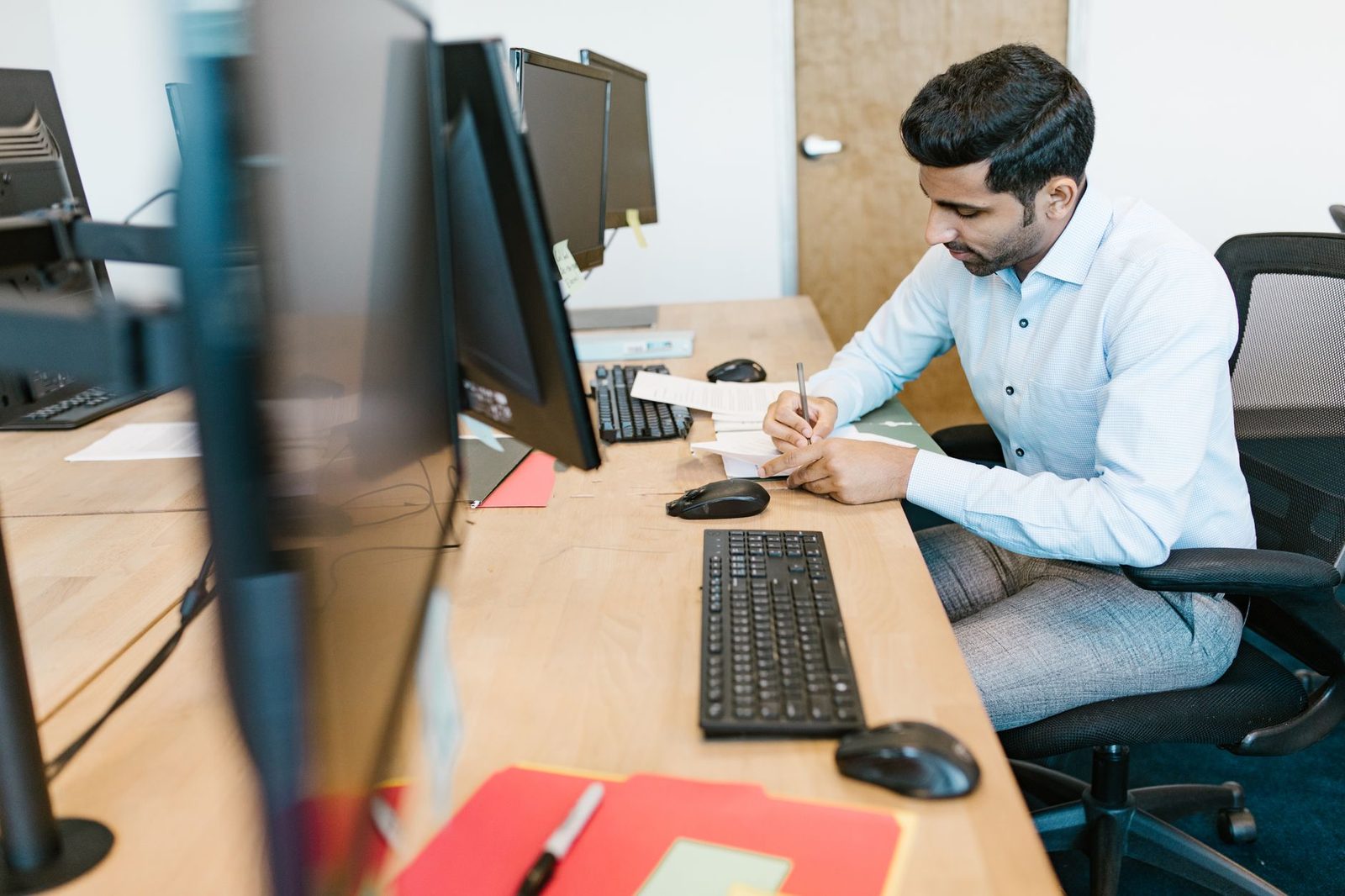 Business professional reviewing paperwork at a multi-monitor office desk