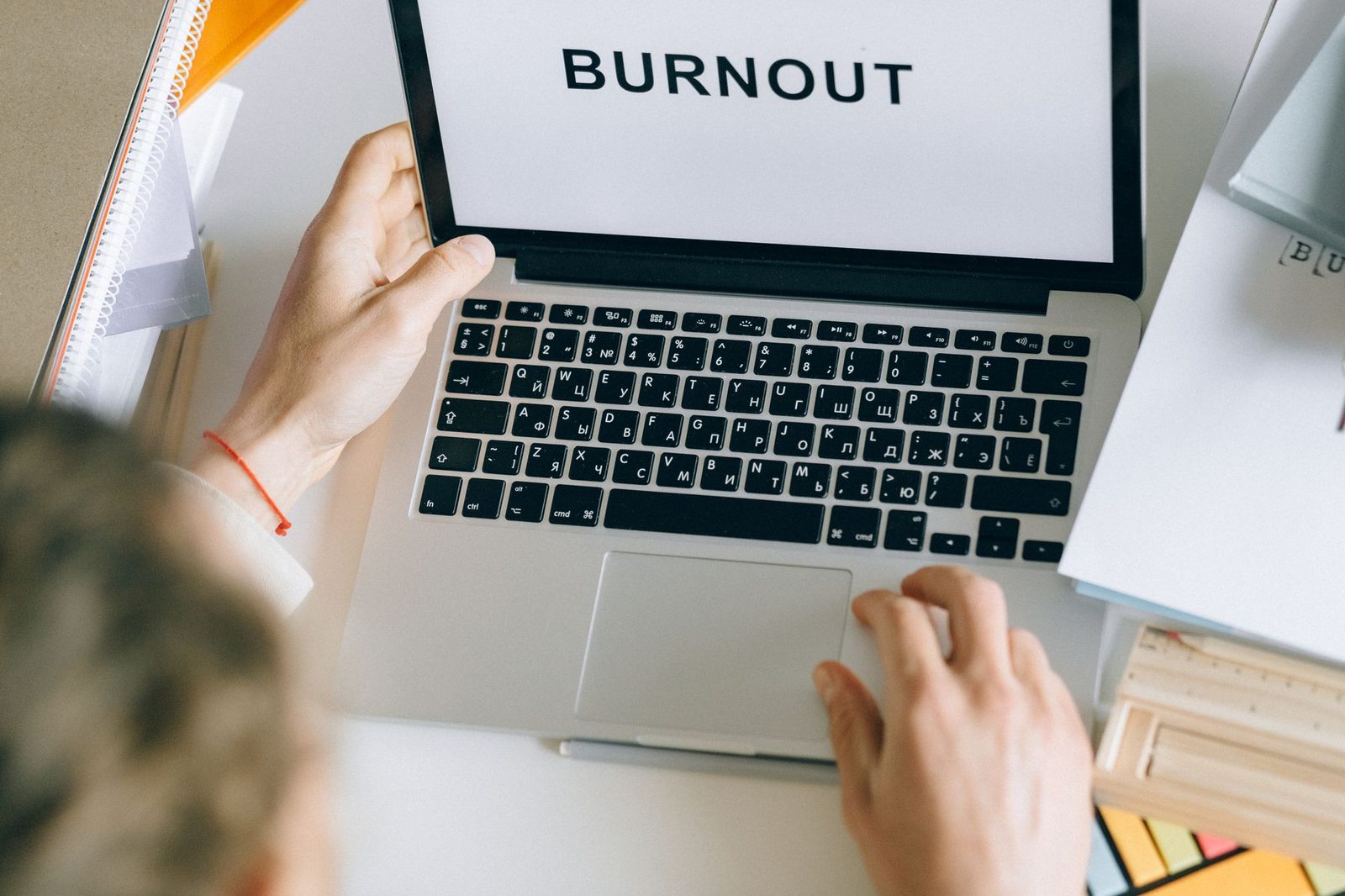 Laptop screen displaying the word BURNOUT while someone works at a desk